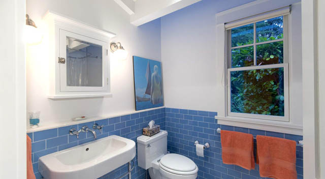 Bright bathroom with blue tiles and orange accents, featuring a window with a view of greenery. - 235 Maple Lane, West Vancouver
