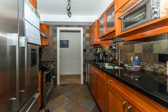 Compact kitchen with dark countertops, wooden cabinets, and a tiled backsplash. - 409 - 1500 Hornby Street, Vancouver Downtown