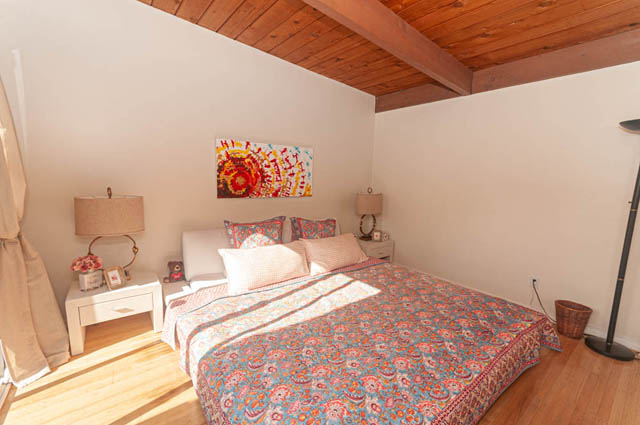 Spacious bedroom with hardwood floors, wooden beams, and colorful patterned bedding. - 85 Glenmore Drive, West Vancouver