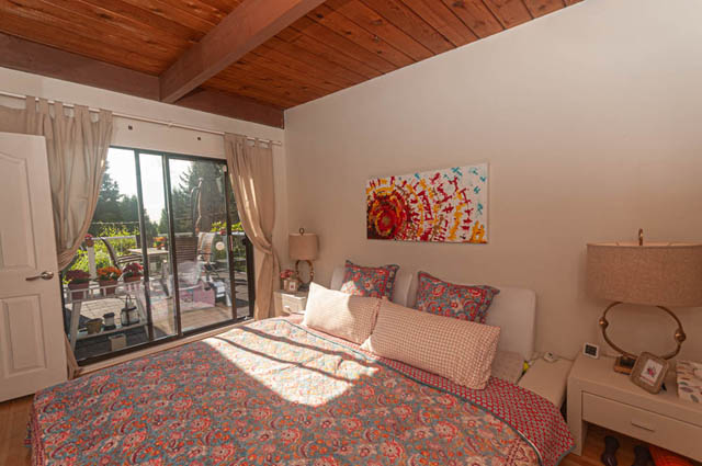 Spacious bedroom with wooden ceiling, large windows, and vibrant floral bedding. - 85 Glenmore Drive, West Vancouver