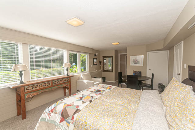 Spacious bedroom with patchwork quilt, large windows, and cozy seating area. - 85 Glenmore Drive, West Vancouver