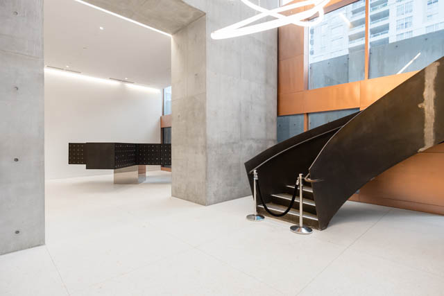 Modern open-concept living room with concrete walls and a sleek black staircase. - 1901 - 1480 Howe St, Vancouver Downtown