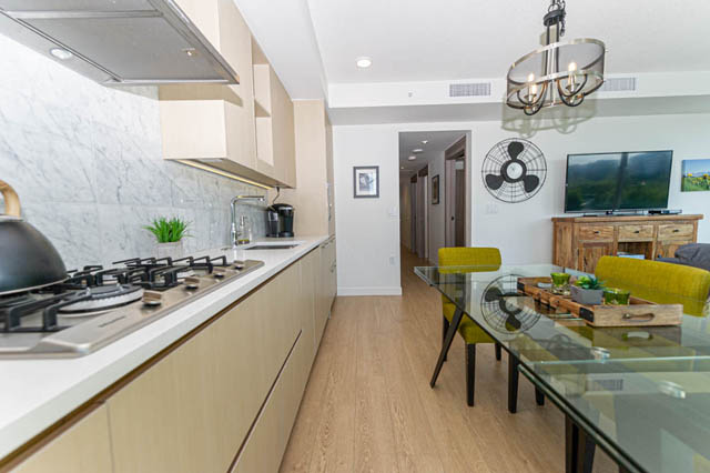 Bright kitchen with modern appliances and marble countertops, leading to a cozy living area with a TV and fan.
