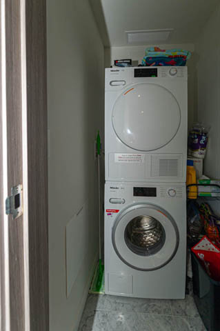 Laundry room with stacked washer and dryer, white countertops, and small storage items. - 484 - 87 Nelson St, Vancouver Downtown