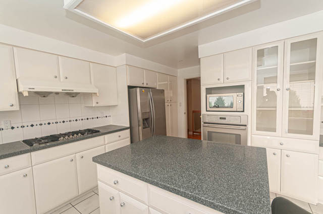 Bright kitchen with white cabinets, granite countertops, and a stainless steel refrigerator. - 669 Eyremount Drive, West Vancouver