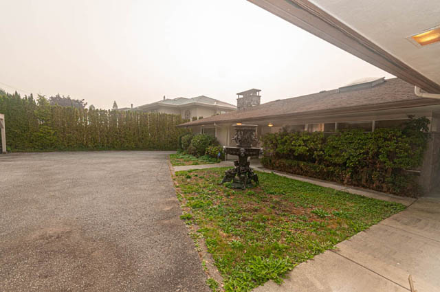 Large open driveway leading to a 5-bedroom house with a well-maintained garden and a modern house in the background.
