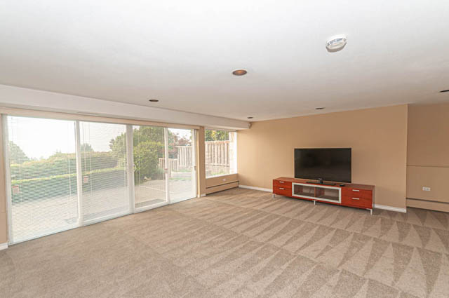 Spacious living room with large windows, carpeted floor, and flat-screen TV. - 669 Eyremount Drive, West Vancouver