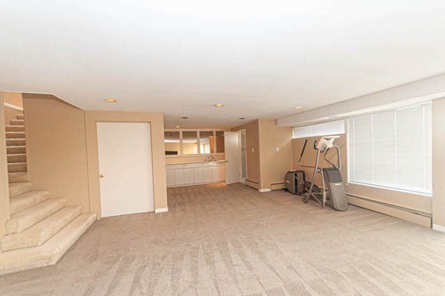 Open living room with carpeted floors and large windows, leading to a kitchen area. - 669 Eyremount Drive, West Vancouver