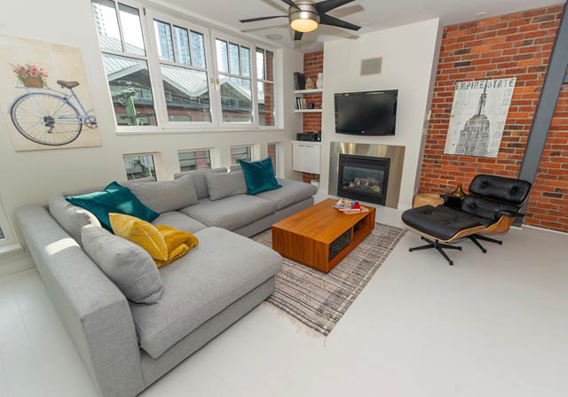 Bright living room with brick accent wall, modern furniture, and large windows. - 410 - 1072 Hamilton St, Vancouver Downtown