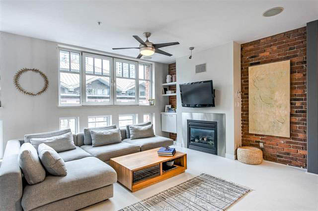 Furnished living room with brick accent wall and modern TV setup. - 410 - 1072 Hamilton St, Vancouver Downtown