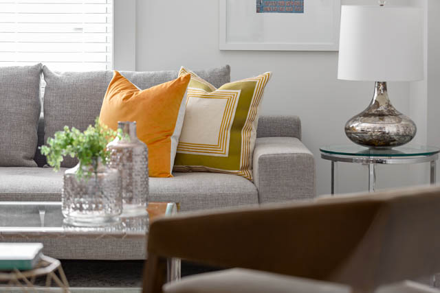 Bright living room with modern furnishings, orange and yellow throw pillows, and a sleek glass coffee table.