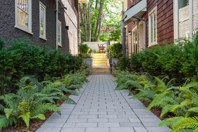 Furnished patio with stone pavers, lush greenery, and a yellow-stairway entrance. - 201 - 1785 W 16th Avenue, Vancouver West Side