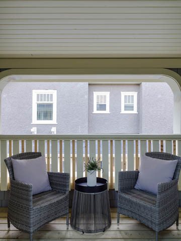 Furnished balcony with wicker chairs and a small table, overlooking a building with white windows. - 3170 Burrard St, Vancouver West Side