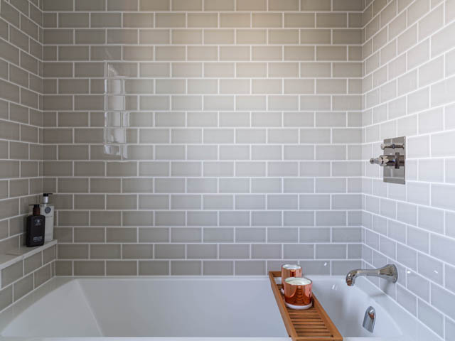 Spacious bathroom with white subway tiles and a wooden bath caddy holding candles. - 3170 Burrard St, Vancouver West Side