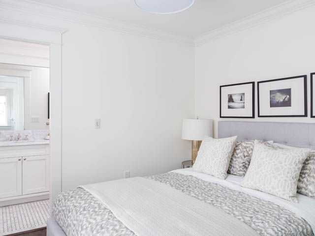 Furnished bedroom with white walls, patterned bedding, and a bathroom in the background. - 3170 Burrard St, Vancouver West Side