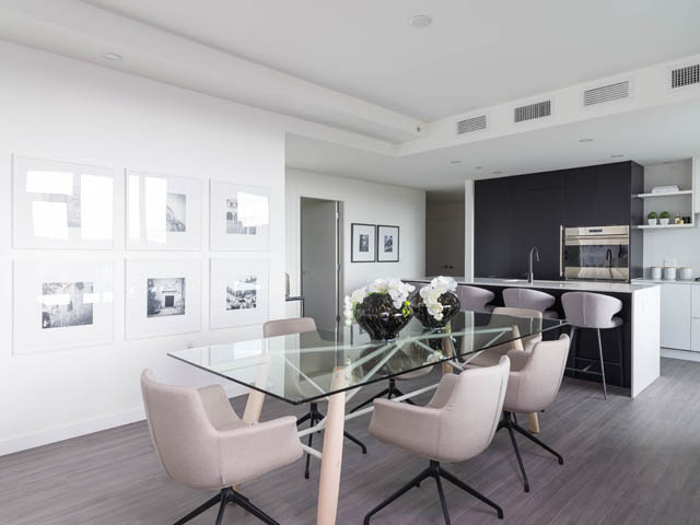 Bright dining area with modern chairs and glass table, leading to a sleek kitchen with black cabinetry and stainless...