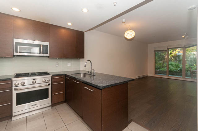 Bright kitchen with dark wood cabinets, granite countertops, and a view of greenery outside. - 117 - 3478 Westbrook Mall, Vancouver West Side