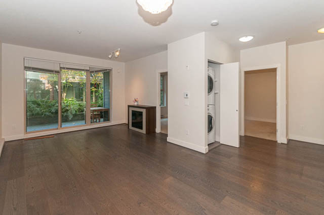 Open-concept living room with hardwood floors and sliding glass doors leading to an outdoor area. - 117 - 3478 Westbrook Mall, Vancouver West Side