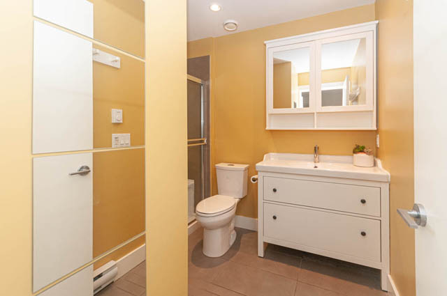 Furnished bathroom with white vanity, yellow walls, and a toilet. - 117 - 3478 Westbrook Mall, Vancouver West Side