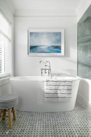 Bright bathroom with white freestanding tub, black and white checkered floor, and artwork above the tub.