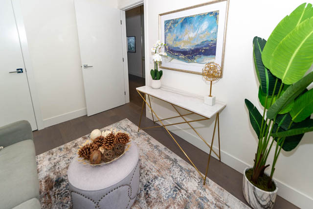 Foyer with marble console table, abstract art, and large green plant, leading to a cozy living area with a patterned rug...