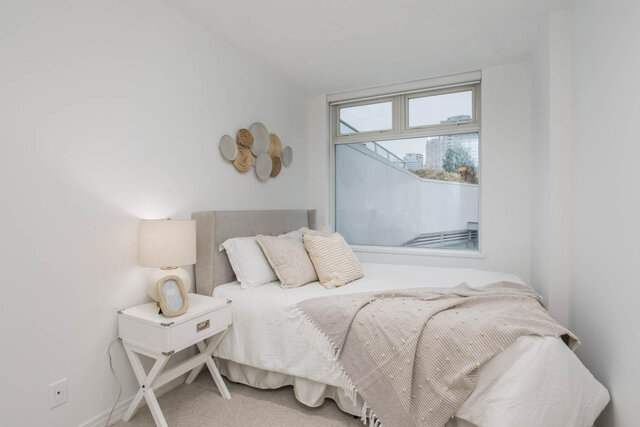 Spacious bedroom with a cozy bed, neutral decor, and a large window offering a city view. - THA - 1199 Marinaside Cres, Vancouver Downtown