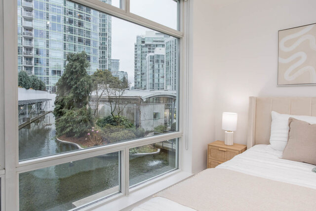 Spacious bedroom with large windows offering a stunning city view and a serene water feature outside. - THA - 1199 Marinaside Cres, Vancouver Downtown