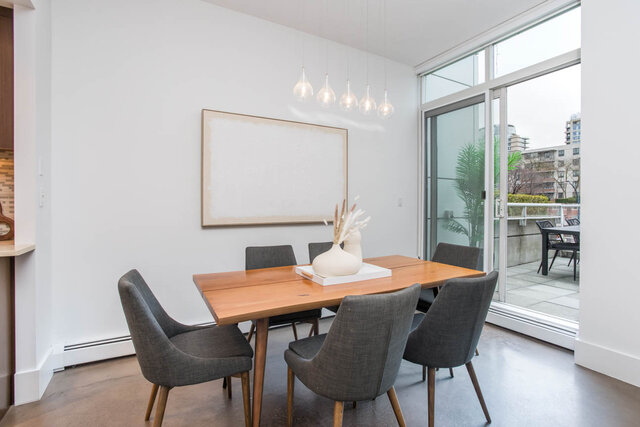 Modern dining area with sleek wood table, gray chairs, and large window view of cityscape. - THA - 1199 Marinaside Cres, Vancouver Downtown