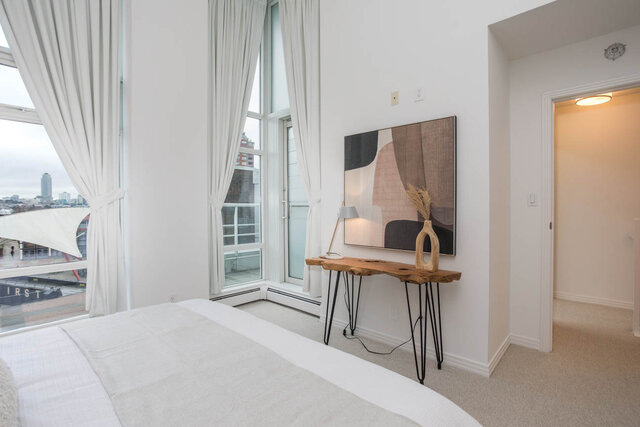 Spacious bedroom with a city view and modern artwork, featuring a sleek desk and cozy bedding. - THA - 1199 Marinaside Cres, Vancouver Downtown