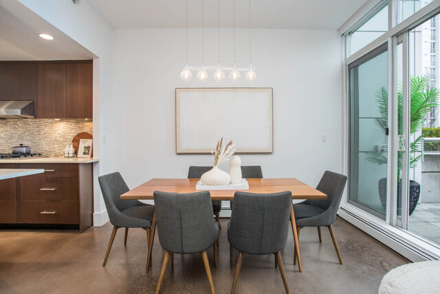 Modern dining room with sleek wood table, gray chairs, and pendant lights, overlooking a cityscape. - THA - 1199 Marinaside Cres, Vancouver Downtown