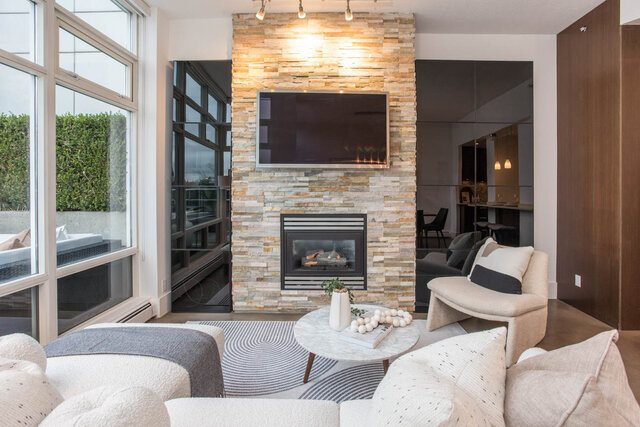 Spacious living room with a stone fireplace, modern TV, and cozy seating area. - THA - 1199 Marinaside Cres, Vancouver Downtown