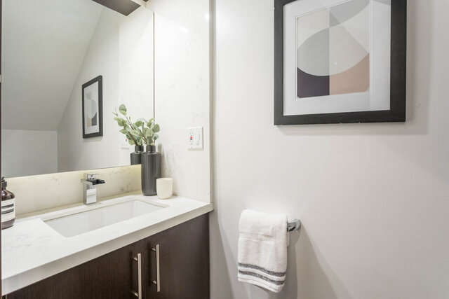 Modern bathroom with sleek white countertops and stylish artwork above the toilet. - THA - 1199 Marinaside Cres, Vancouver Downtown