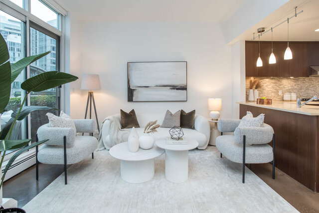 Modern living room with white couch, geometric coffee table, and city view through large windows. - THA - 1199 Marinaside Cres, Vancouver Downtown