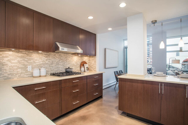 Modern kitchen with sleek wood cabinets, white countertops, and a city view. - THA - 1199 Marinaside Cres, Vancouver Downtown