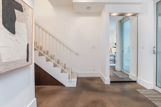 Modern entryway with concrete flooring, white walls, and a staircase leading to the upper levels. - THA - 1199 Marinaside Cres, Vancouver Downtown