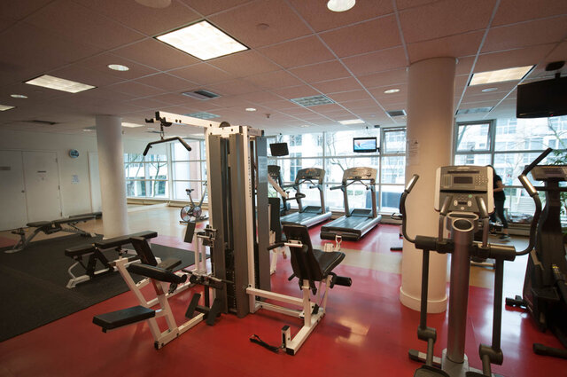 Spacious fitness room with cardio machines, weightlifting equipment, and large windows offering a city view.