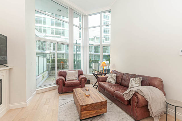 Bright living room with large windows, hardwood floors, and city view. - 105 - 199 Victory Ship Way, North Vancouver