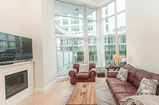 Bright living room with hardwood floors, city view, and cozy leather sofa. - 105 - 199 Victory Ship Way, North Vancouver