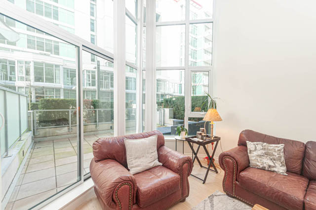 Furnished living room with large windows, city view, and modern decor. - 105 - 199 Victory Ship Way, North Vancouver