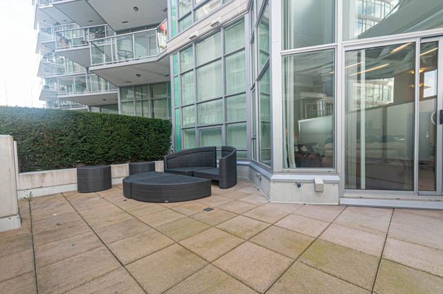 Furnished patio with modern furniture and glass doors leading to the interior. - 105 - 199 Victory Ship Way, North Vancouver