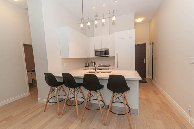 Bright kitchen with white cabinets, hardwood floors, and modern bar stools. - 105 - 199 Victory Ship Way, North Vancouver