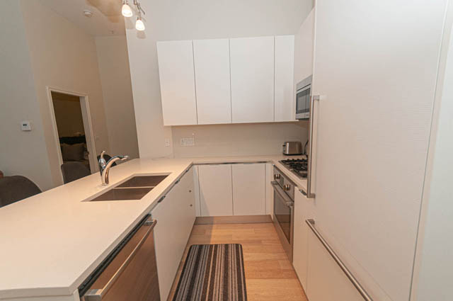 Bright kitchen with white cabinets, hardwood floors, and a modern sink setup. - 105 - 199 Victory Ship Way, North Vancouver