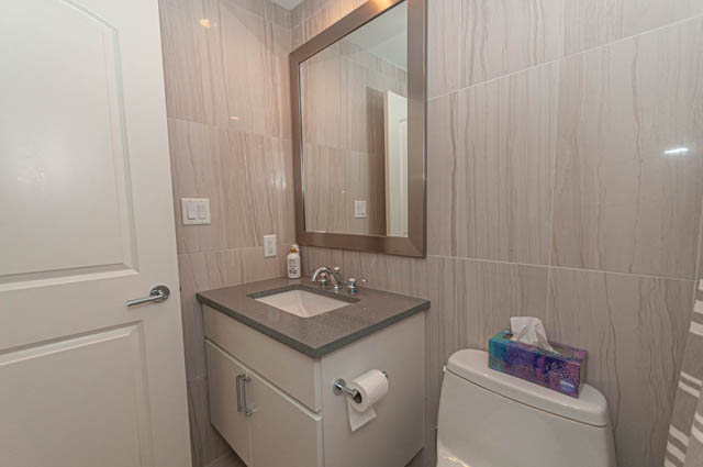 Bright bathroom with modern sink, large mirror, and light-colored tiles. - 105 - 199 Victory Ship Way, North Vancouver
