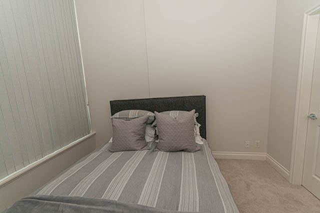 Furnished 1-bedroom bedroom with striped carpet and gray headboard. - 105 - 199 Victory Ship Way, North Vancouver