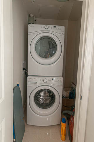 Laundry room with stacked washer and dryer, white cabinets, and cleaning supplies. - 105 - 199 Victory Ship Way, North Vancouver