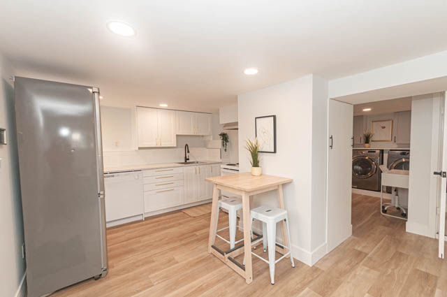 Bright kitchen with white cabinets, hardwood floors, and a modern stainless steel refrigerator. - Suite - 522 5th St E, North Vancouver
