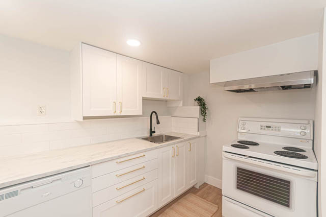 Bright kitchen with white cabinets, marble countertops, and stainless steel appliances. - Suite - 522 5th St E, North Vancouver