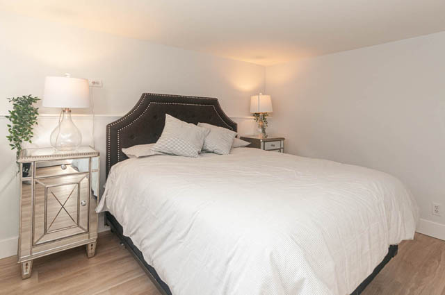 Furnished bedroom with white bedding and mirrored nightstands. - Suite - 522 5th St E, North Vancouver