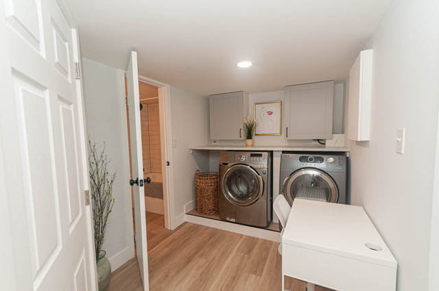 Bright laundry room with white cabinets, hardwood floors, and a laundry machine. - Suite - 522 5th St E, North Vancouver