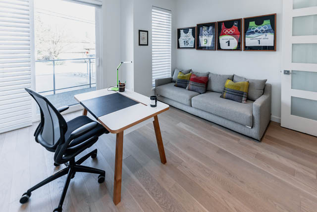 Bright living room with hardwood floors and a modern office setup, featuring a gray sofa and a sleek desk. - Address WITHHELD, North Vancouver